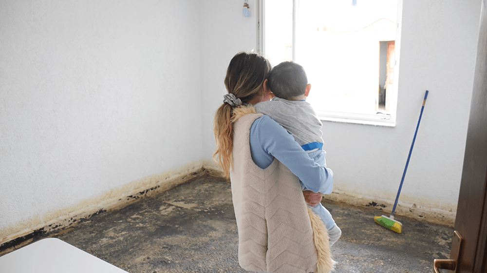 Young mother with 8 month old baby standing in a destoyed house from flooding