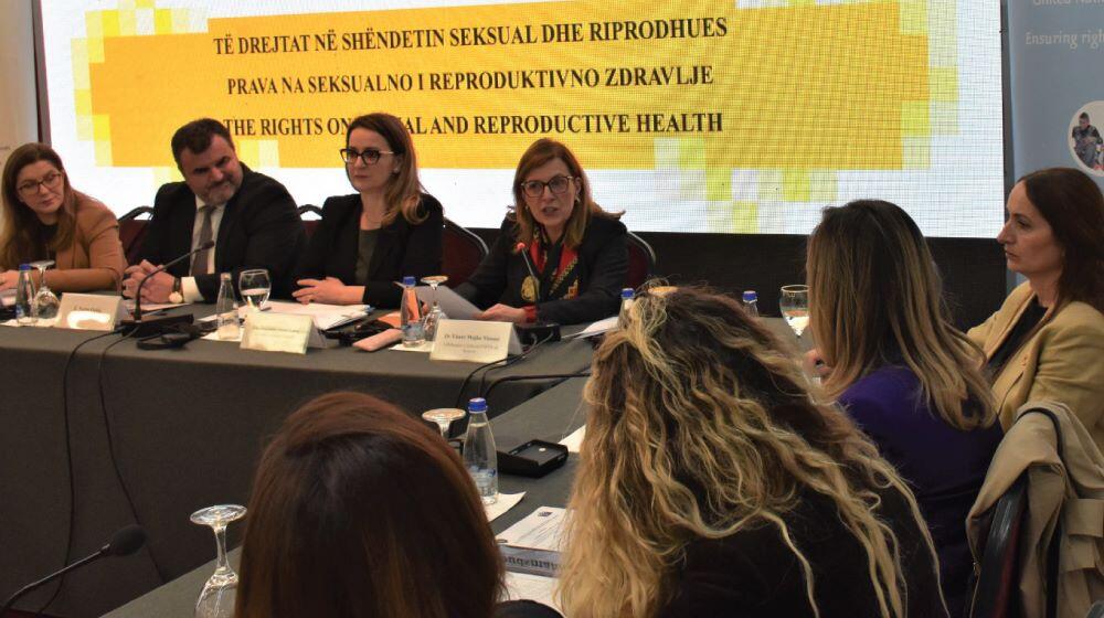 A panel discussion at a conference featuring two women and two men. One of the women is speaking, others listening