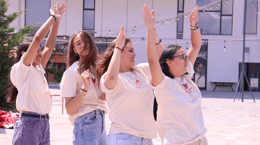 Four young women rstanding in a row while raing hands